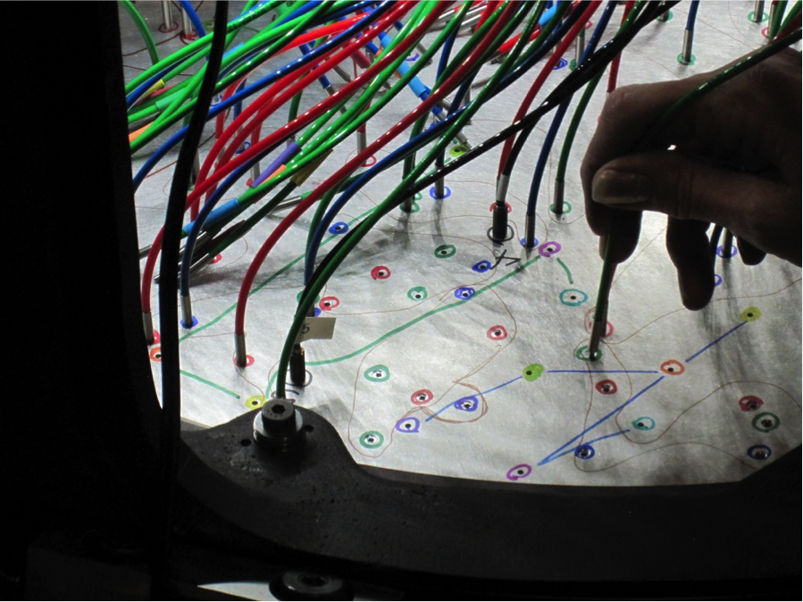  Prior to the observation of a plate, fibers are hand-plugged into pre-drilled holes and the fibers are then mapped by shining a laser on the slithead to determine which fibers correspond to which holes (and therefore to which stars). Here, an APOGEE-North fiber is plugged into a plate. Each hole on a plate corresponds to a single object on the sky and the different colored fibers denote faint, medium and bright targets.  <em>Photo courtesy of J. Wilson.</em> 