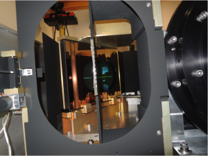 A view inside the APOGEE-South instrument looking towards the pseudo-slit.  The VPH grating can be seen in reflection focused on Fold Mirror 2.  The Camera barrel is to the right. <em>Photo courtesy of J. Wilson.</em> “></a></div>
<div class=