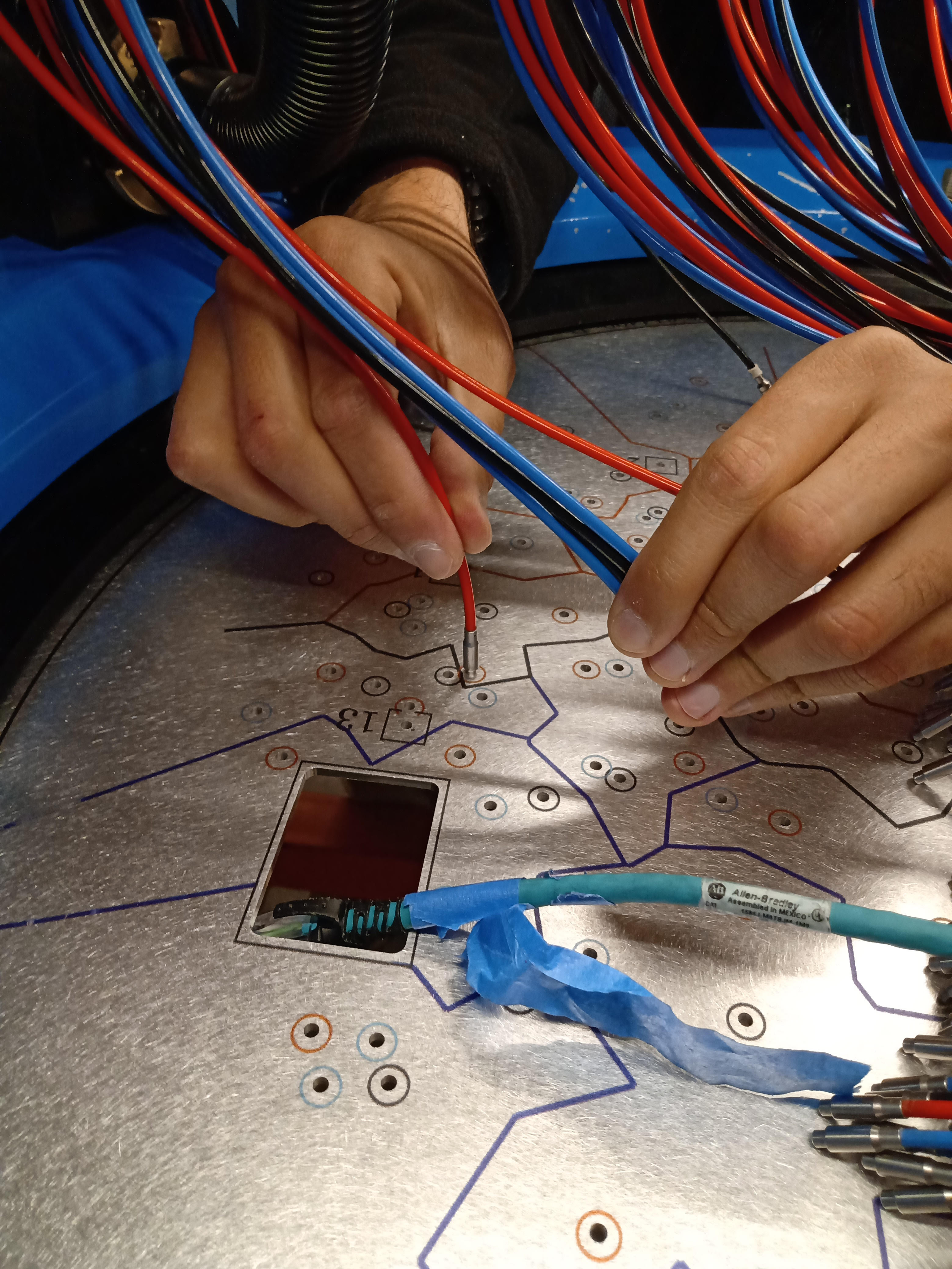 A zoom into the process of connecting the fiber to the plate holes. The APOGEE-2S plates are labeled in a machine process, whereas the plates for APOGEE-2N are labeled by hand. <i> Photo courtesy of A. Almeida </i> 
